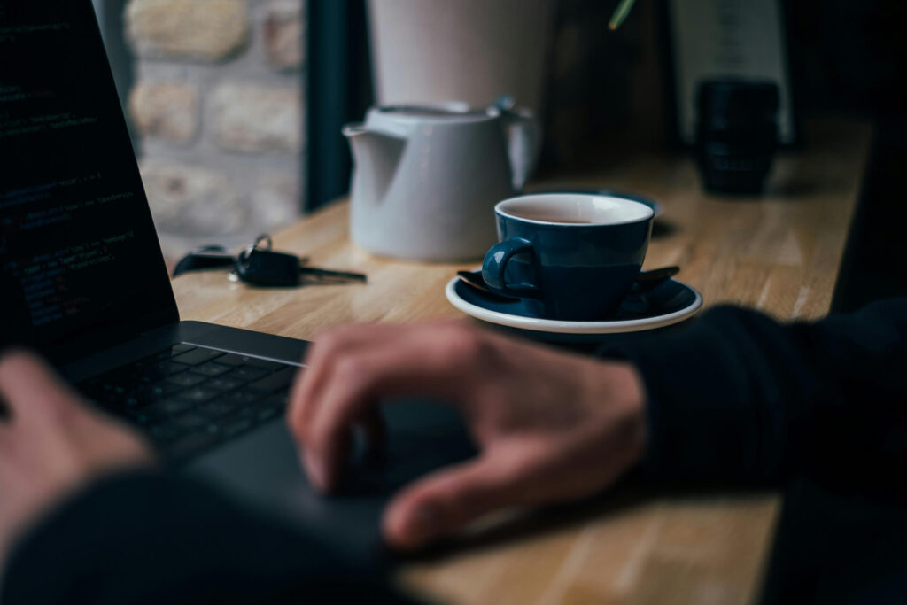 Persona trabajando de forma remota con una laptop en una cafetería, símbolo del trabajo de un asistente virtual.
